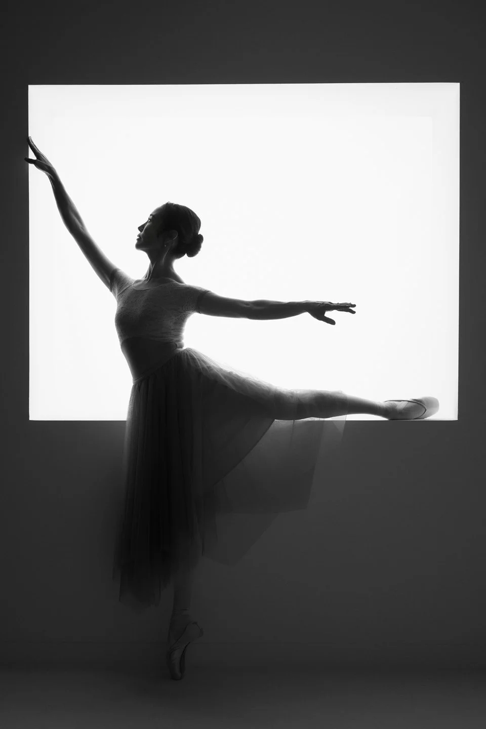 Black-and-white silhouette of Julie holding a ballet pose by a window.
