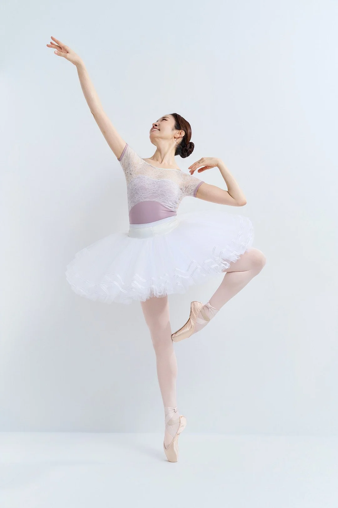 Julie in a white tutu holding a ballet pose against a light studio backdrop.