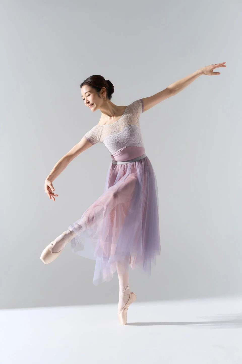 Julie extending her arms in a ballet pose with a lavender skirt.