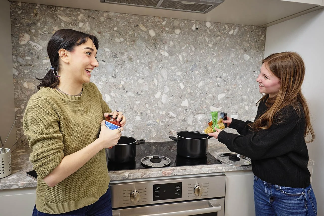 A lifestyle photo of two young women making pasta in the kitchen of a youth hostel in Montreal.