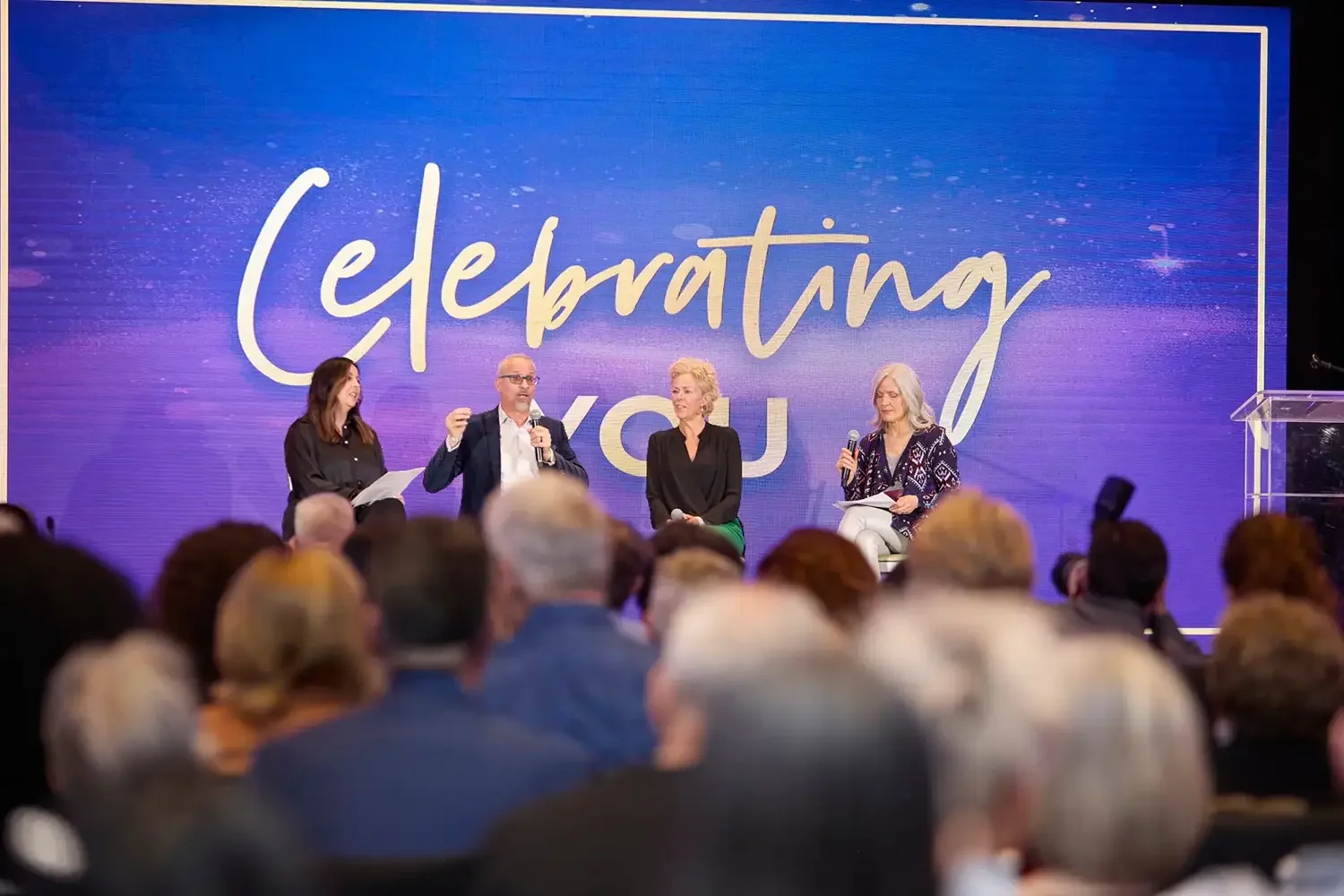 A photo of speakers talking to attendees at a corporate event.