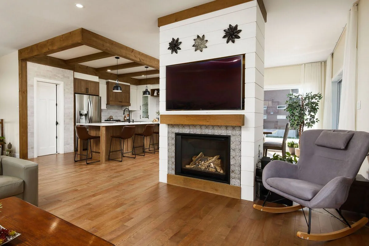 Open-concept living room and kitchen with a fireplace, mounted TV, gray rocking chair, and wooden flooring.