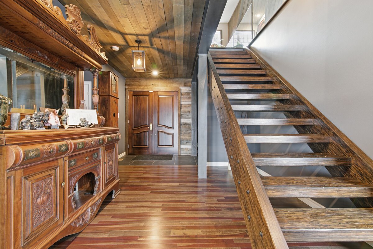 Interior of a house with wooden floors, a staircase on the right, and an ornate wooden sideboard on the left. The entrance door is in the background.