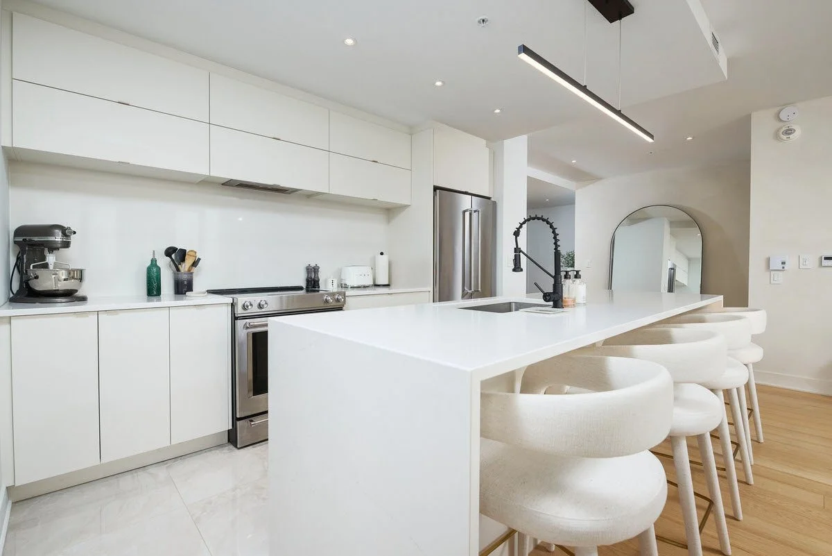 Modern kitchen with white cabinetry, a large white island with barstools, stainless steel appliances, and minimal decor.
