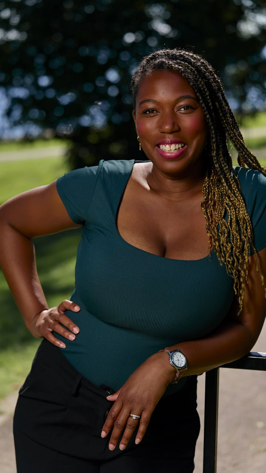 A lifestyle portrait of a woman leaning on a railing and smiling in a park in Montreal.