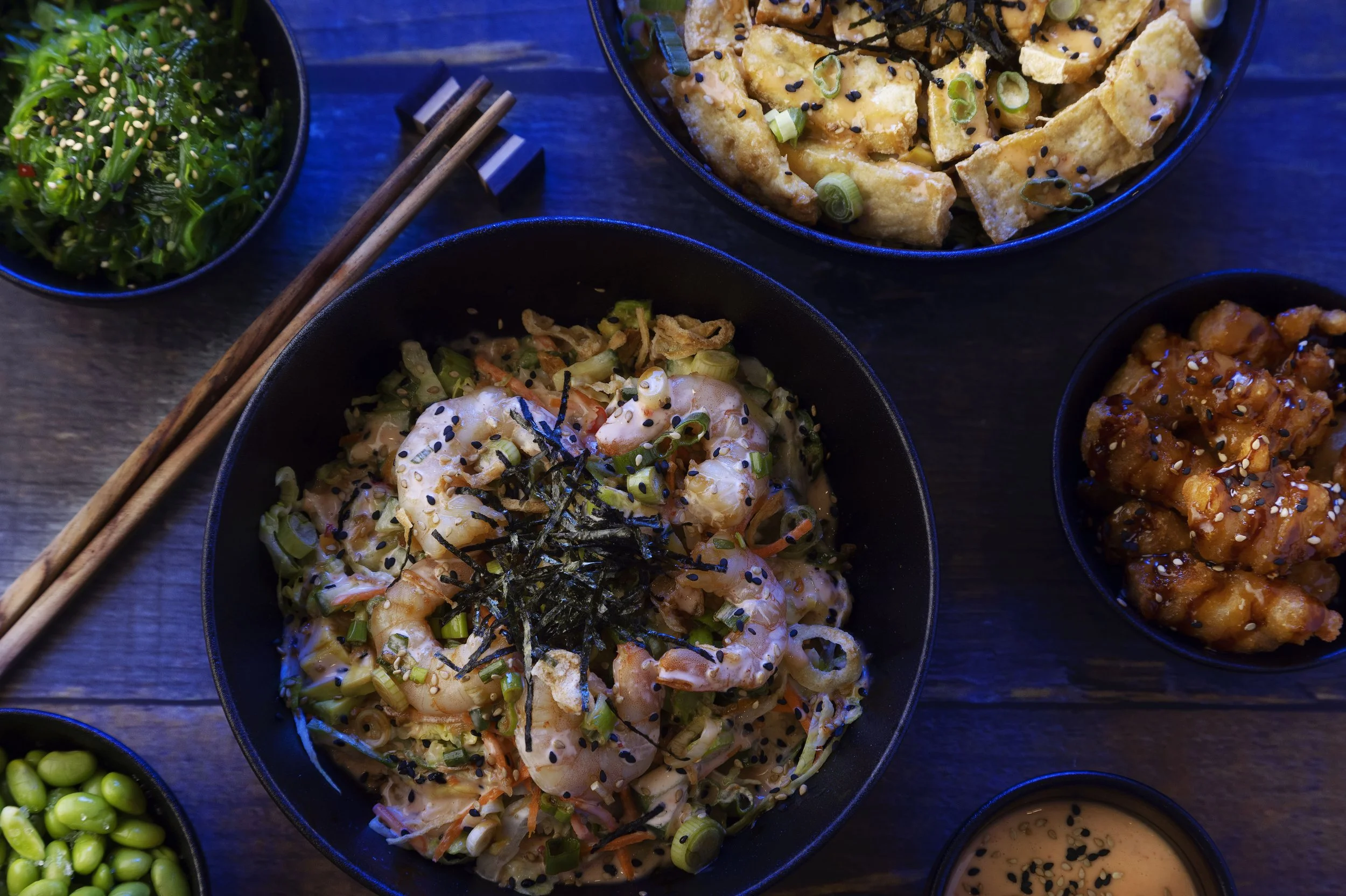 A poké bowl and side dishes with blue light.