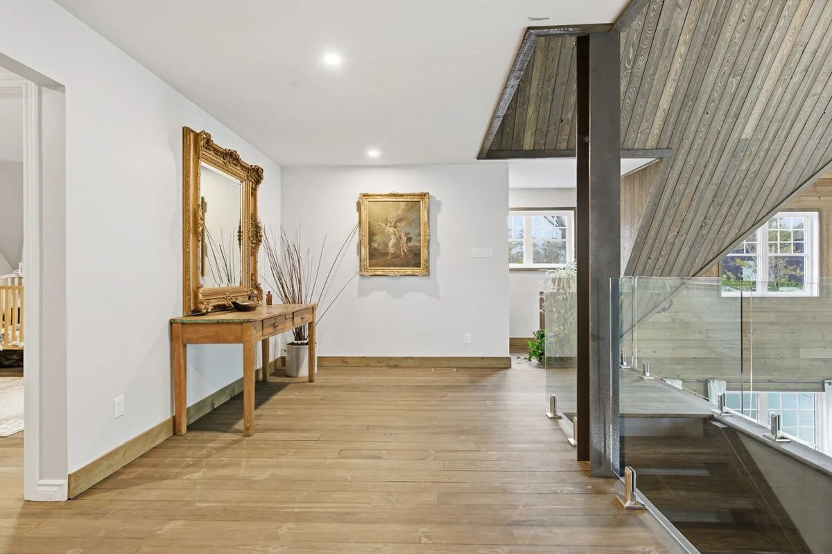 Interior view of a house with wooden floors, white walls, and a staircase with wooden and glass railing.