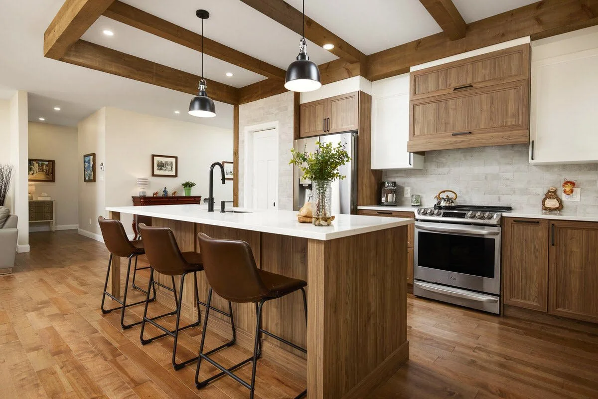 Modern kitchen with wooden cabinets, stainless steel oven, island with white countertop, three brown barstools, and pendant lighting.