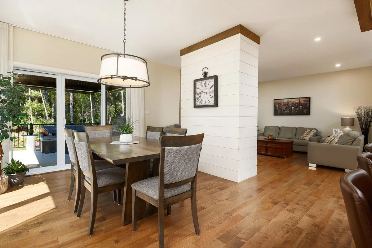 Open living and dining room with wooden floors, a dining table with chairs, a sliding glass door leading to an outdoor patio, sofas with a coffee table, and wall decor.
