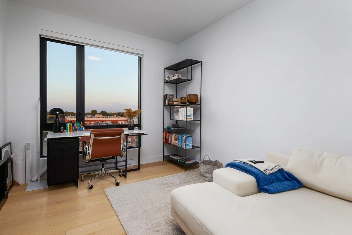 A modern home office with a desk, office chair, bookshelf, and a cream sofa with a blue throw blanket.