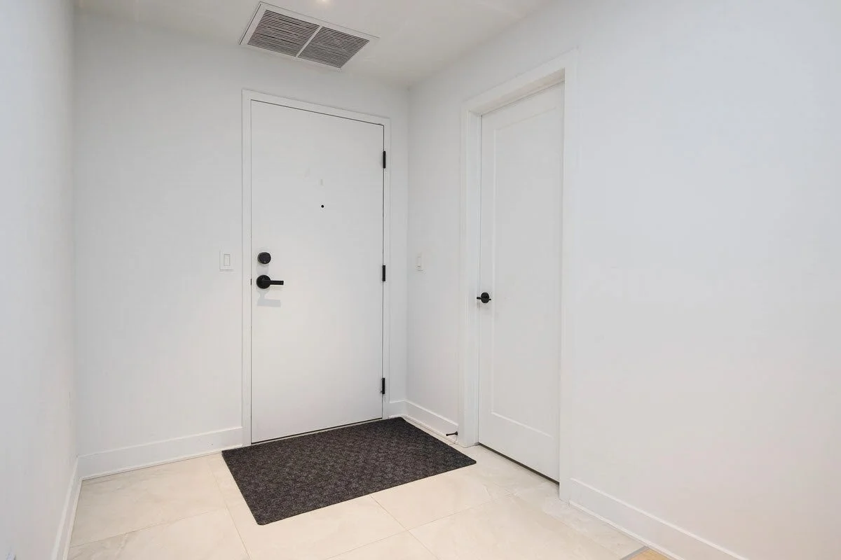 Entryway with white walls, two white doors with black handles, a dark doormat, and a ceiling vent.
