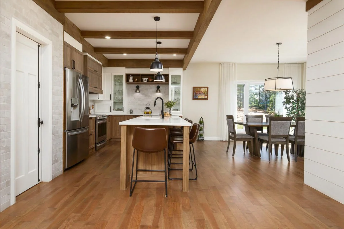 Open kitchen and dining area with wood floors, a kitchen island with brown chairs, and a dining table with chairs by a large window.