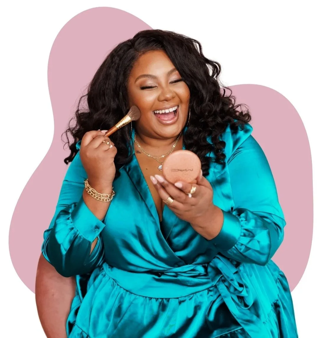 A joyful woman with dark, curly hair applying makeup with a brush while holding a compact mirror, dressed in a bright blue satin robe, jewelry, and smiling.