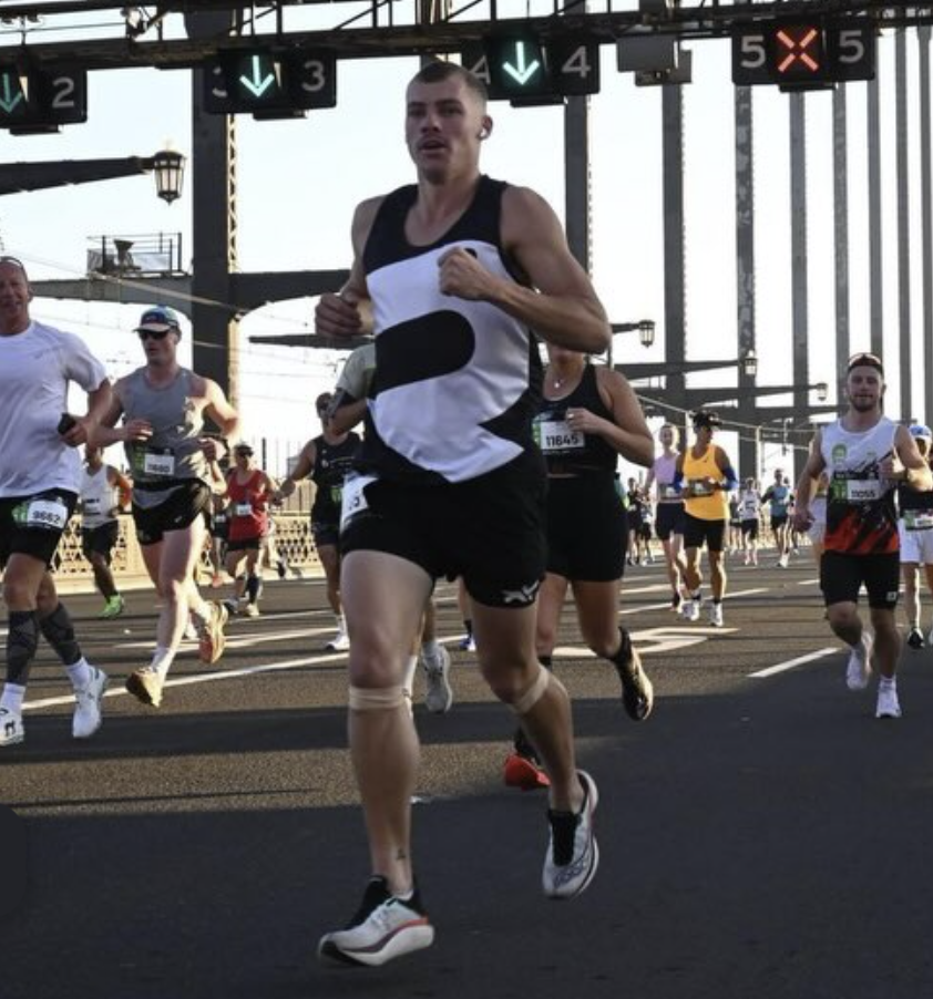 Group of runners participating in a marathon or race on a city street with overhead lanes and digital signboards.
