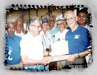 Howard Marx is on the left, receiving a certificate and gift presented by Chuck Thomas. What is being presented was from the original Wright Bicycle Shop that had been torn down. Each shingle from that roof was saved and they had a gold plaque added