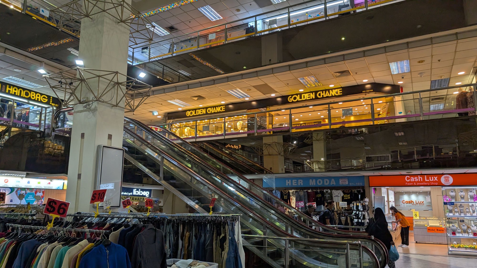 ショッピングモールの内部の画像。複数の階にテナントや店舗があり、エスカレーターとモール内の広告看板が見える。