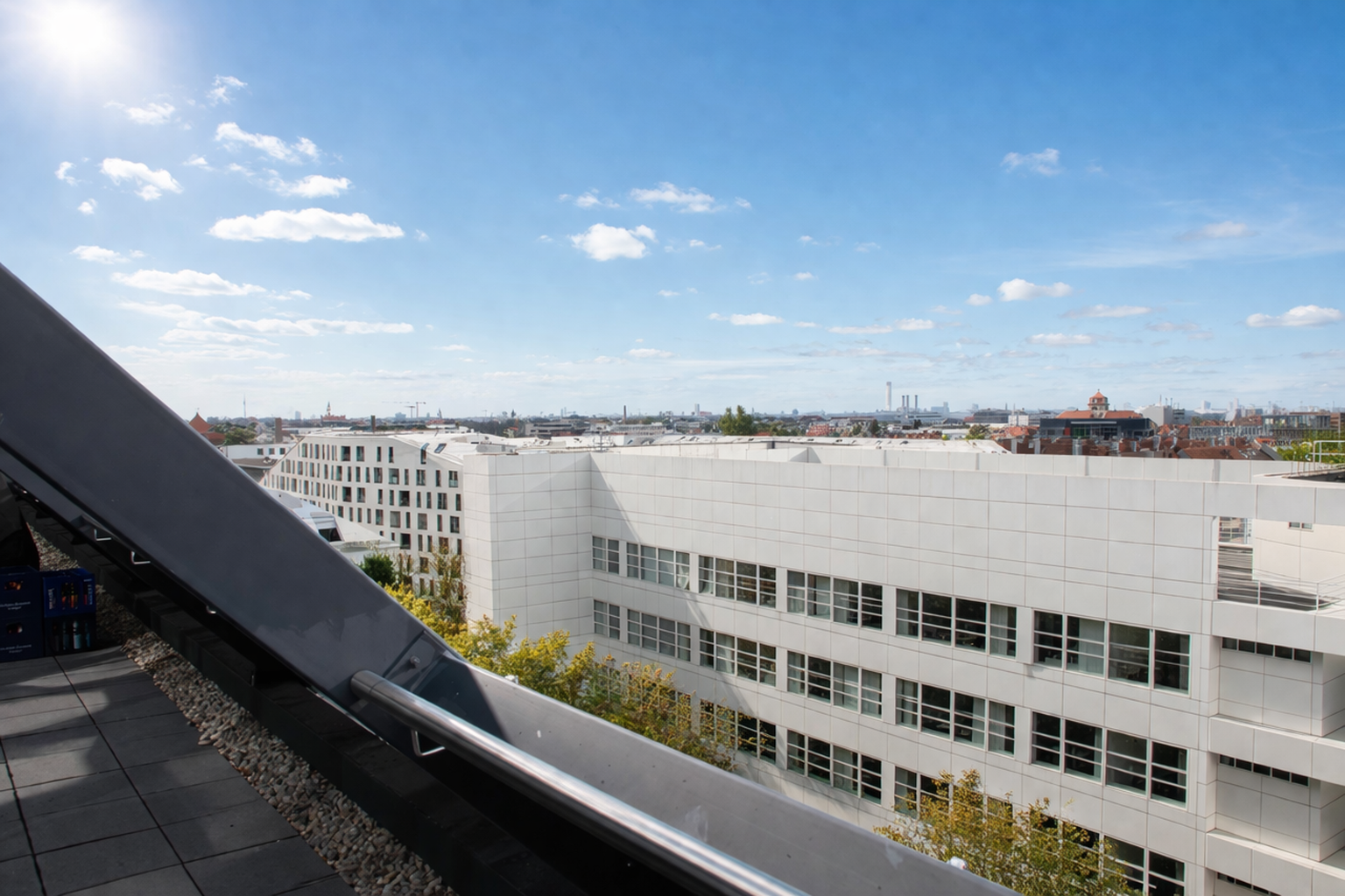 Cityscape view from a rooftop with a modern white building and a bright blue sky with clouds