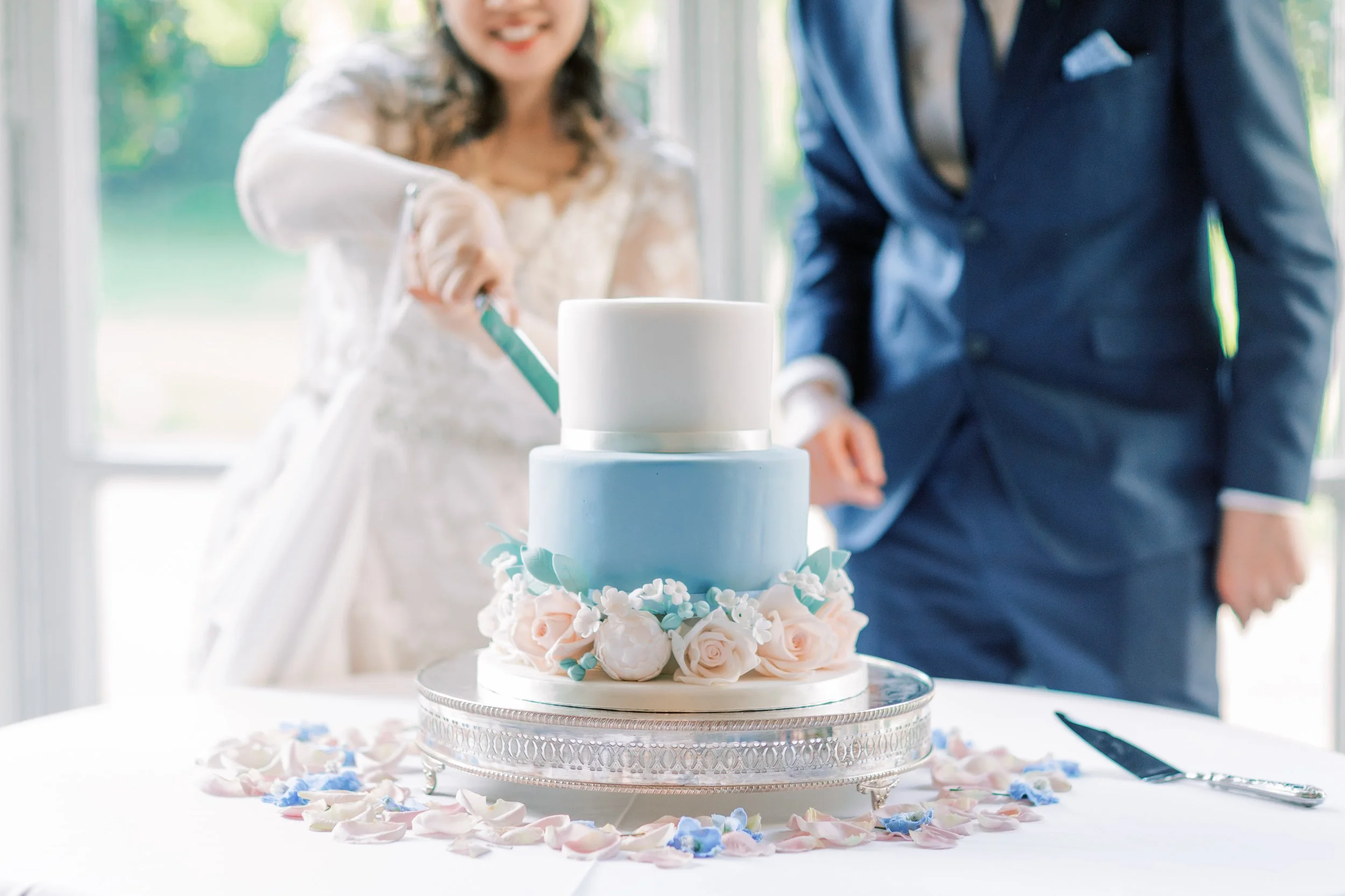 Couple cutting into two tier wedding cake with sugar flowers