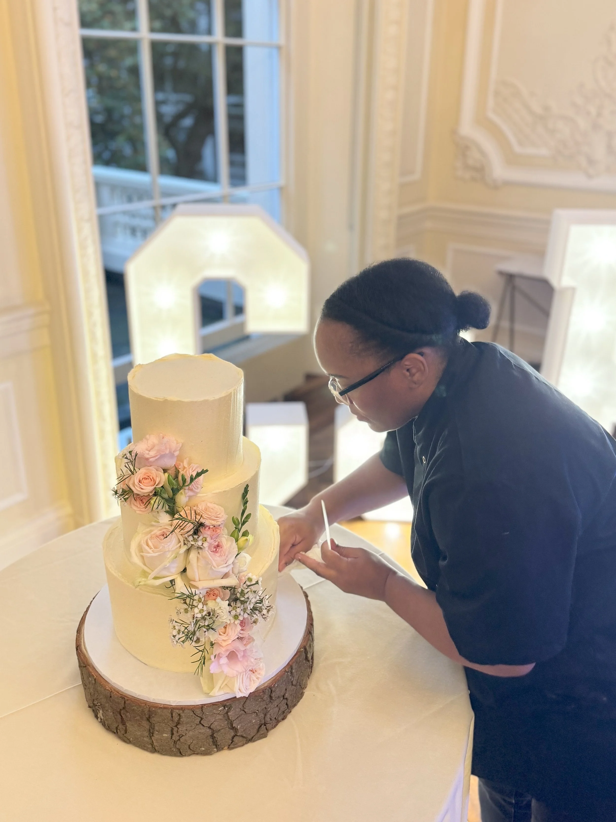 Bianca decorating 3-tier wedding cake with cascading flowers at 10-11 Carlton Terrace wedding venue in London