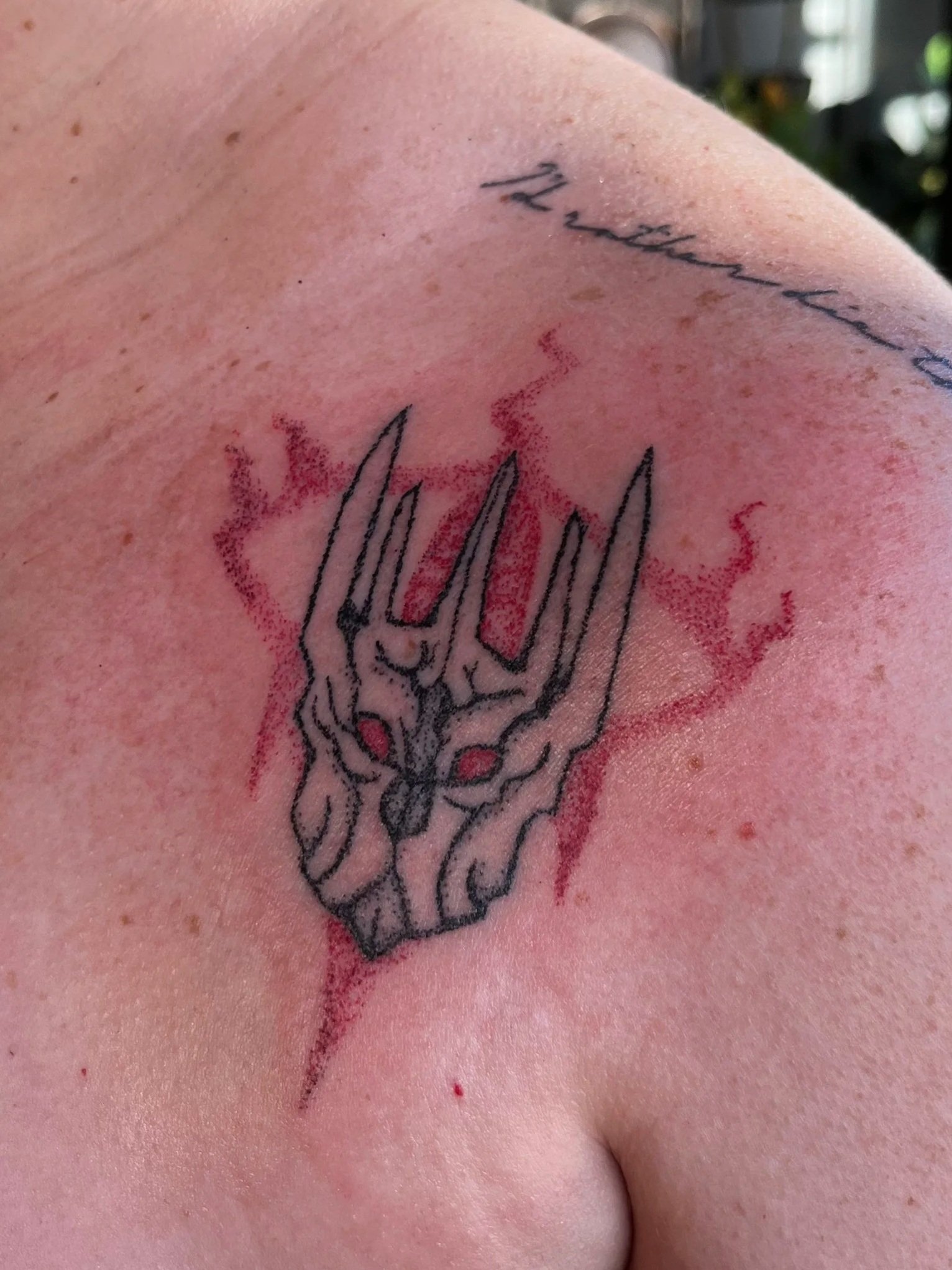 A tattoo on a person's shoulder featuring a hand poked tattoo of Sauron from Lord of the Rings