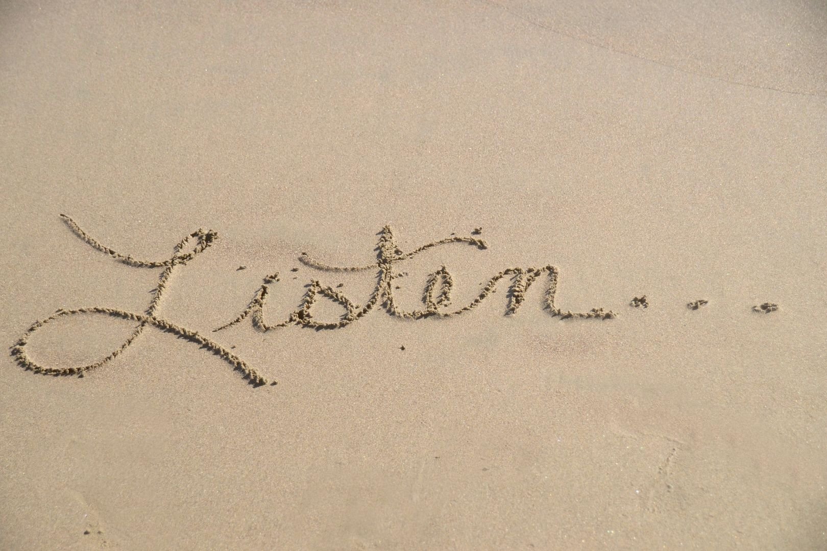 The word listen written in the sand.