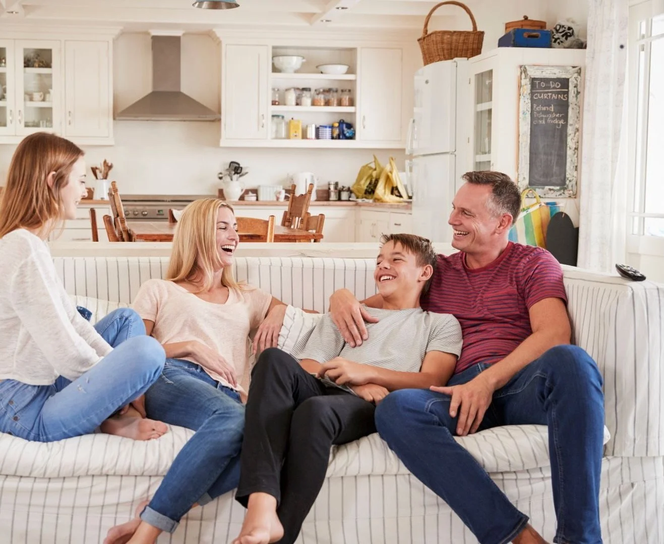 Parents with their teen kids sitting on the coach laughing together.