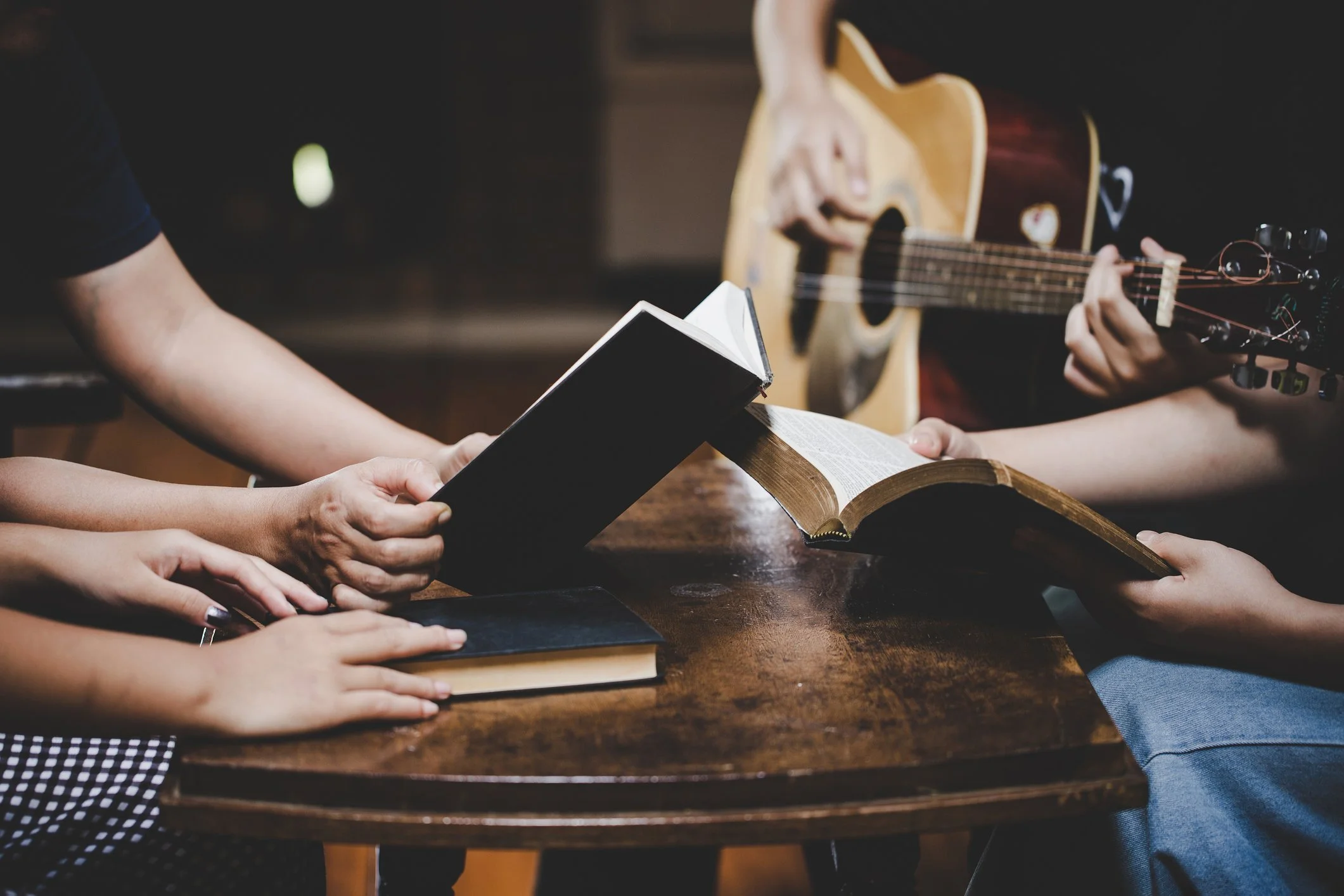 People sitting around a table with books, one person playing an acoustic guitar, and others holding books open. 한인교회, 뉴저지 교회