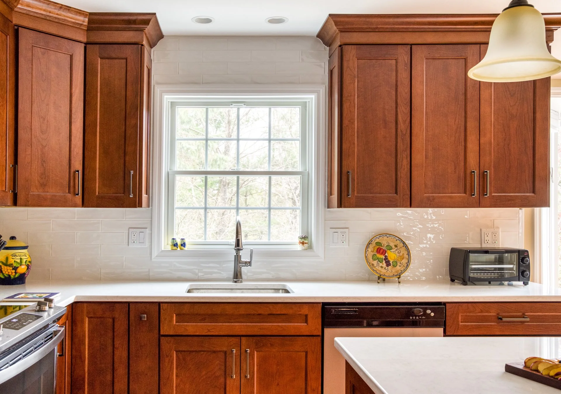 A stunning small kitchen remodel features white countertops, a tiled backsplash and cherry wood cabinetry.