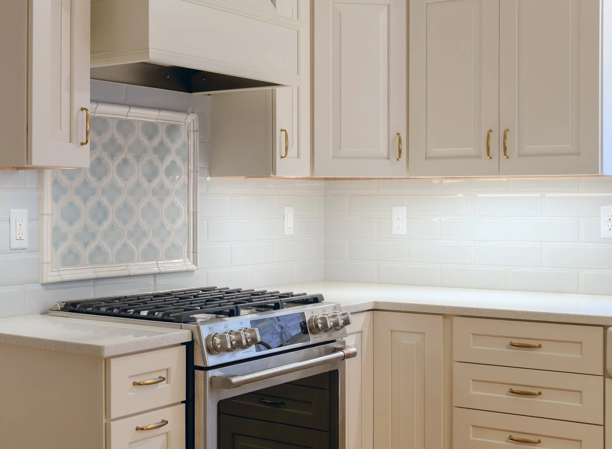 A beautiful small kitchen remodel features white countertops, a tiled backsplash, a stainless steel stove and cream-colored cabinetry.