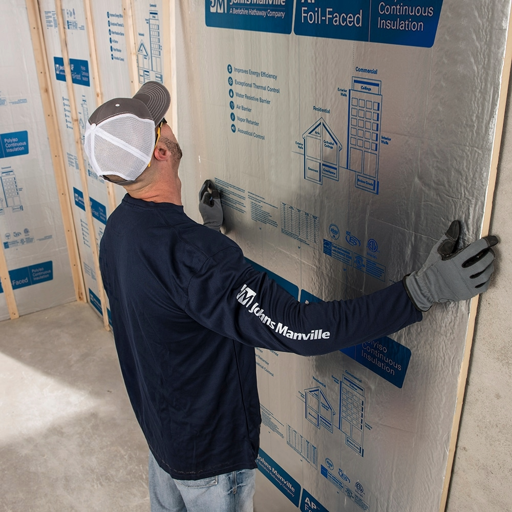Close-up of a worker’s gloved hands pressing Johns Manville ComfortTherm encapsulated fiberglass insulation into a wooden wall frame.