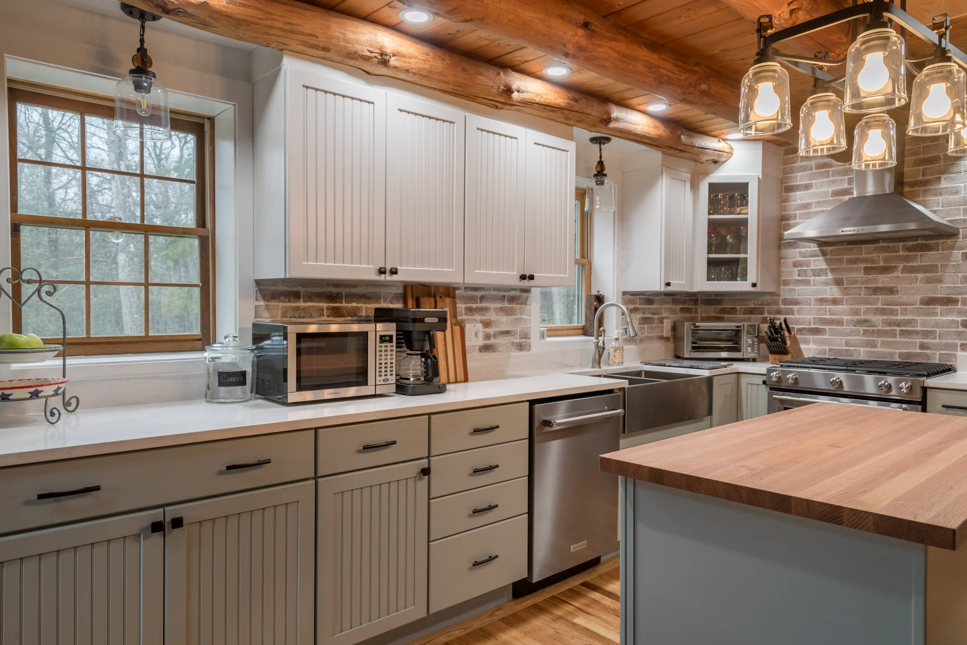 A cabin’s striking small kitchen remodel features white countertops, a butcher block island, white upper cabinetry and green lower cabinetry.