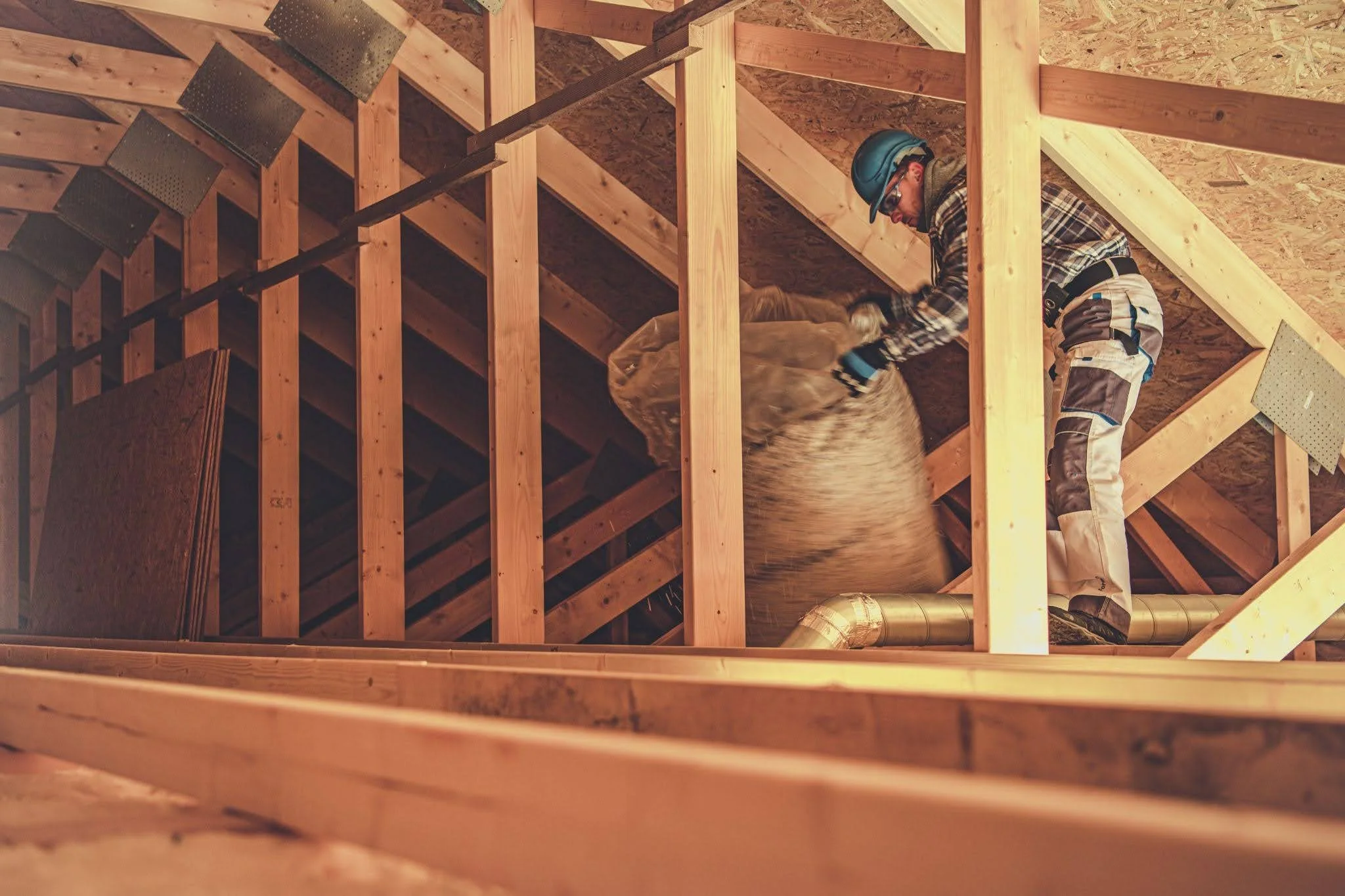 A worker in a Johns Manville shirt installing silver foil-faced rigid foam continuous insulation boards against a wall framing system.