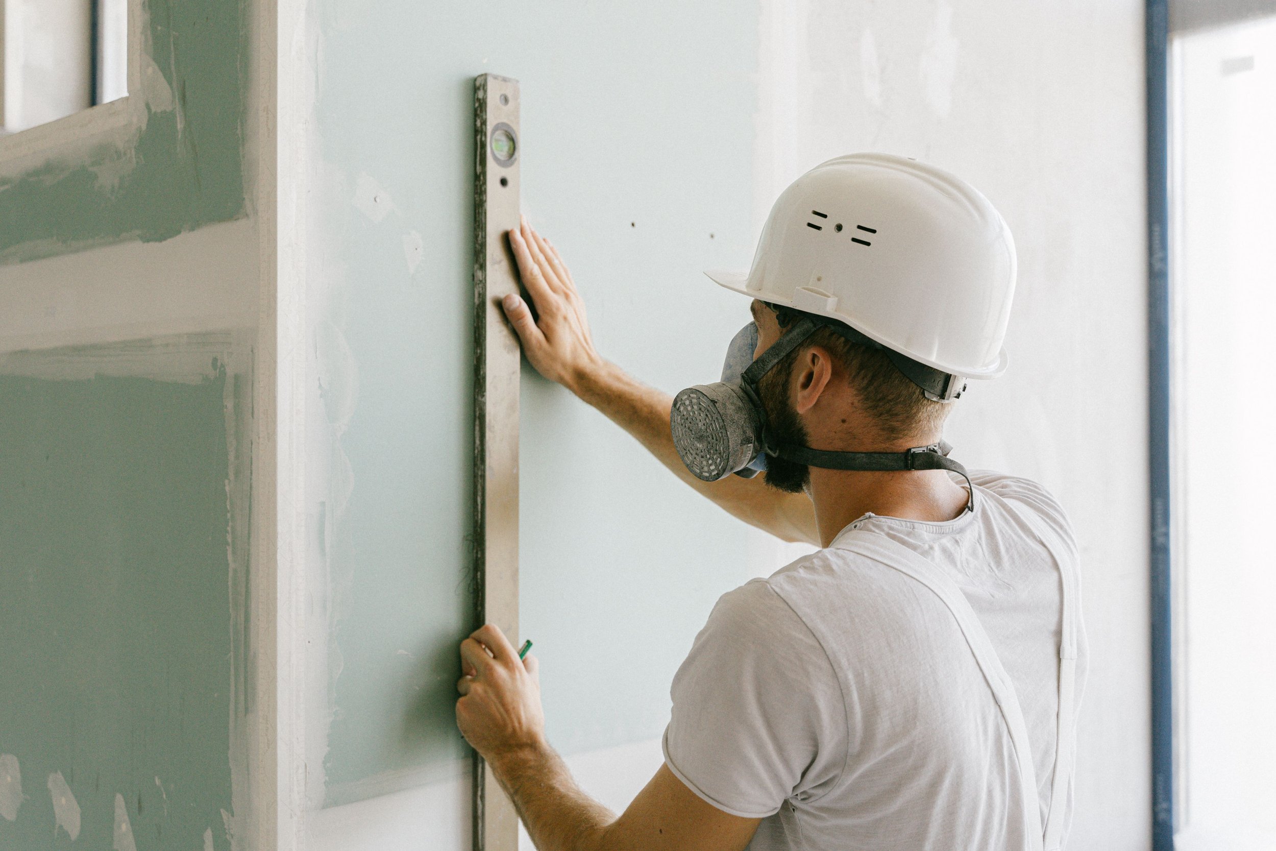 A person wearing PPE is checking to ensure the drywall installation is level.