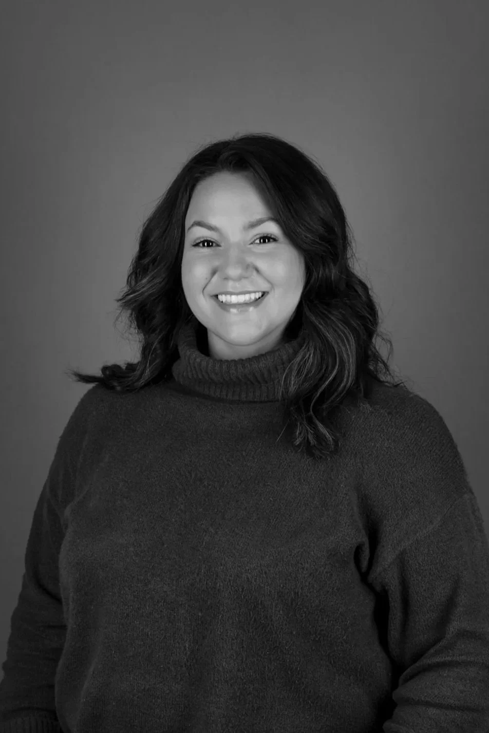 Black and white portrait of a smiling young woman with long hair wearing a black top, against a plain background.
