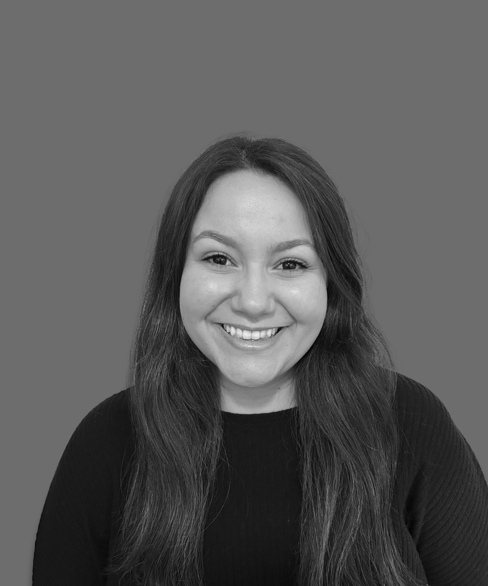 Black and white portrait of a smiling young woman with long hair wearing a black top, against a plain background.