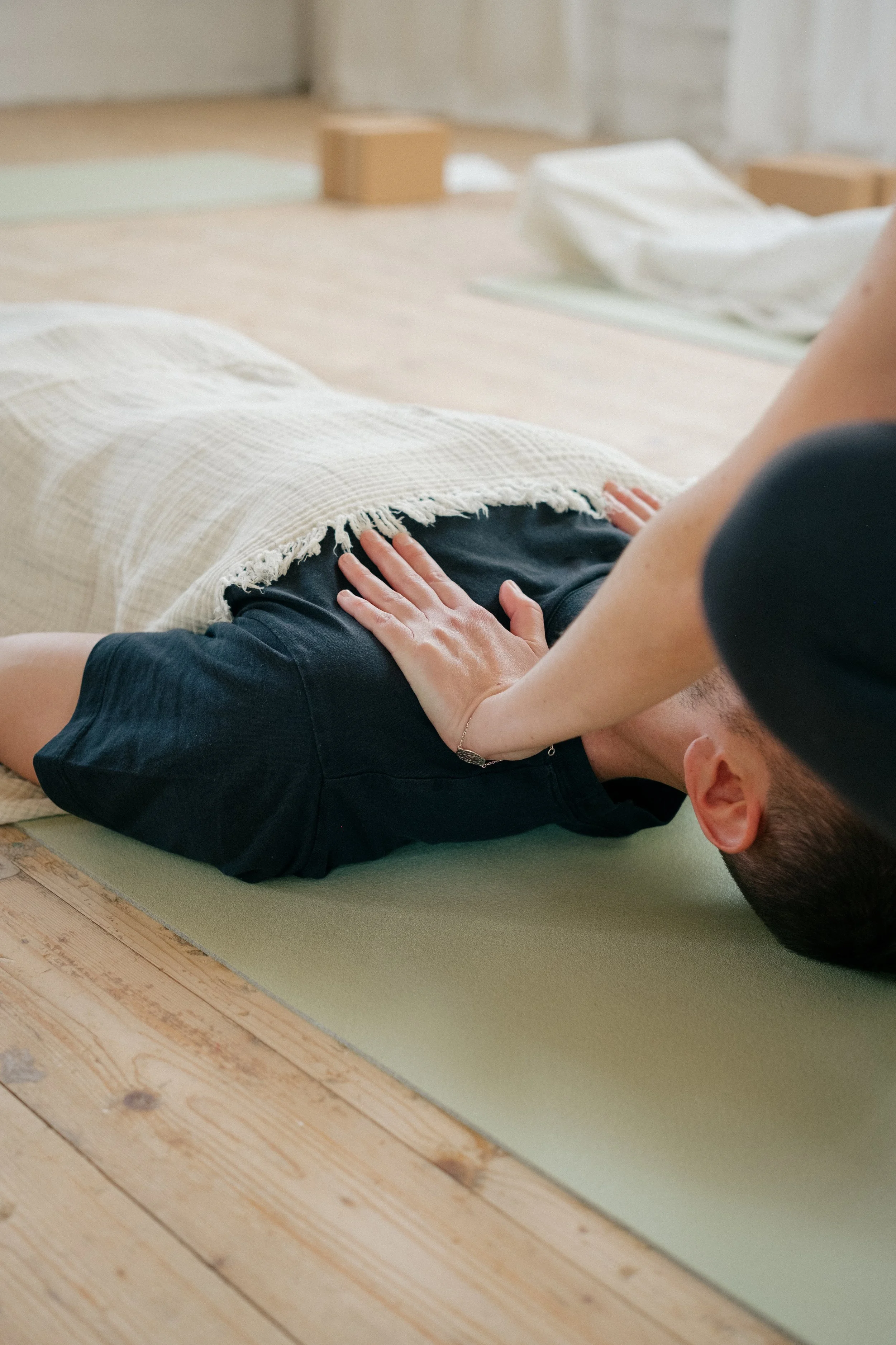 Eine Person erhält eine sanfte Hilfestellung in der Savasana-Entspannungsposition während einer Yogaklasse in Konstanz.