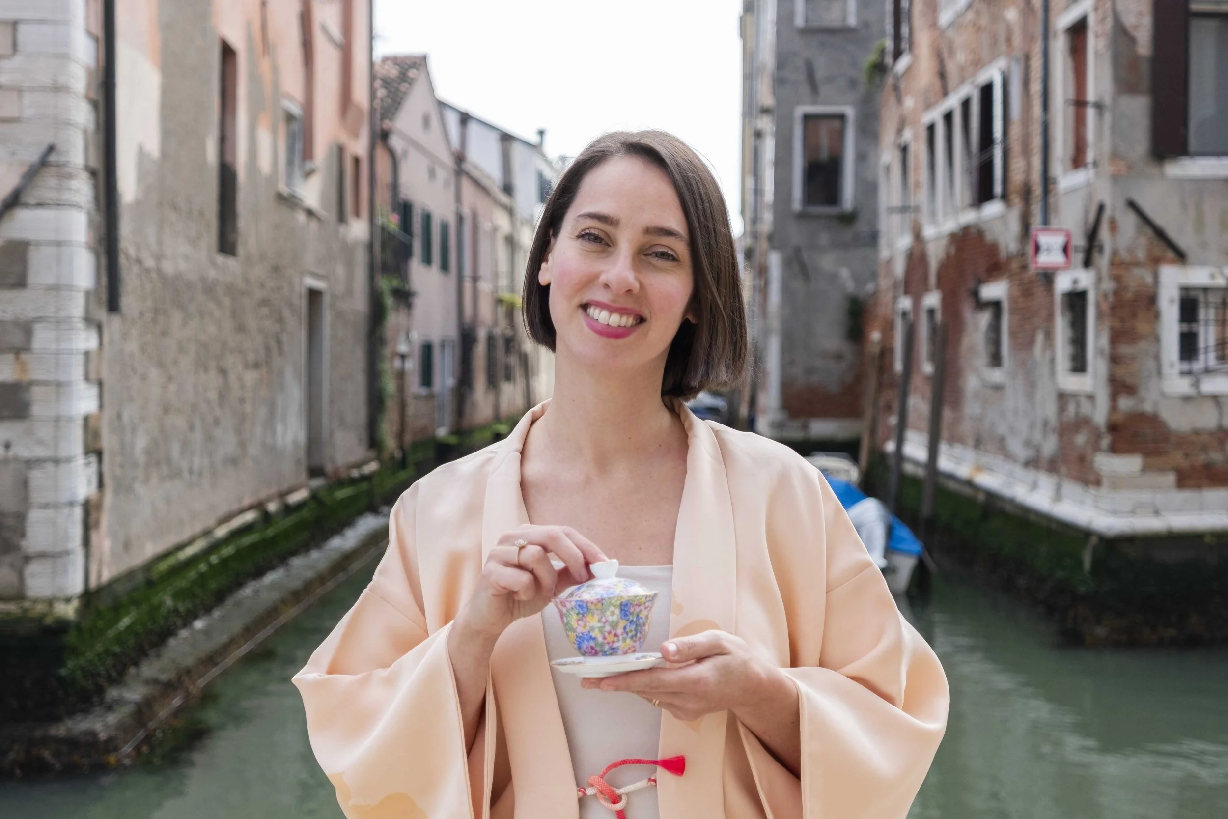 Una donna sorridente tiene in mano una ciotola di cioccolato su un ponte vicino a un canale in un quartiere storico.