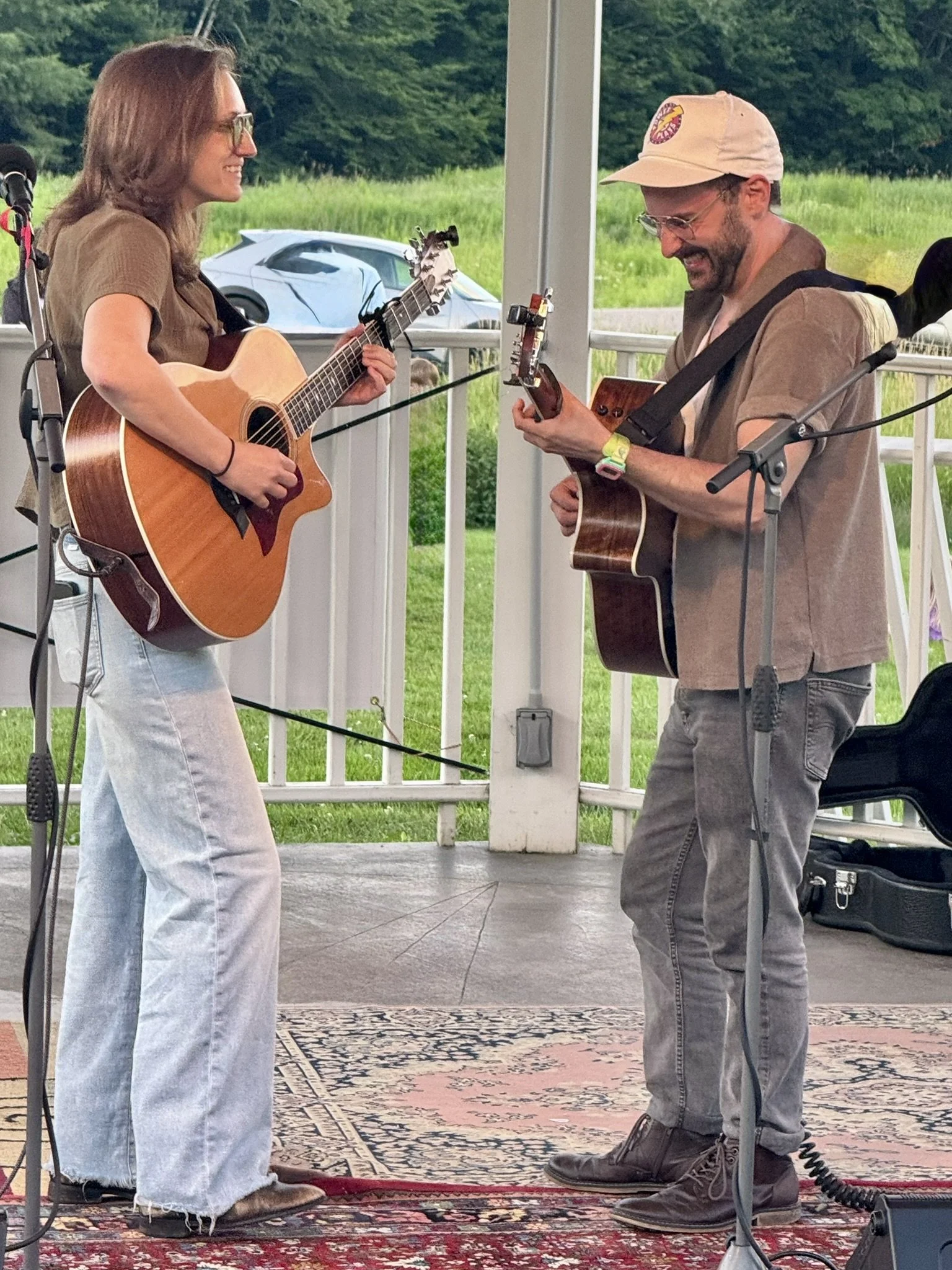 Two musicians playing acoustic guitars and singing on a stage outdoors.