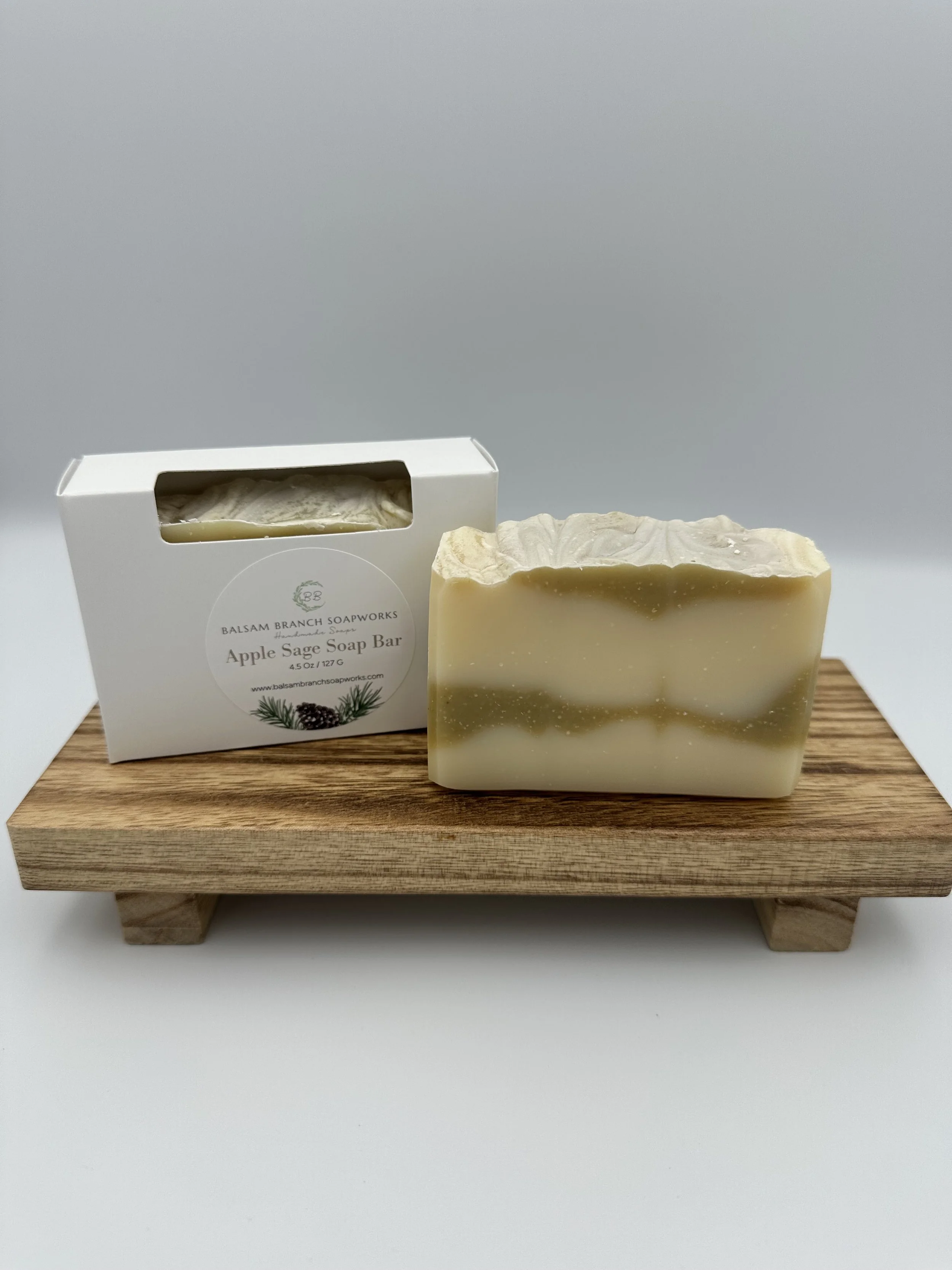 A bar of apple sage soap and its packaging on a wooden display platform.