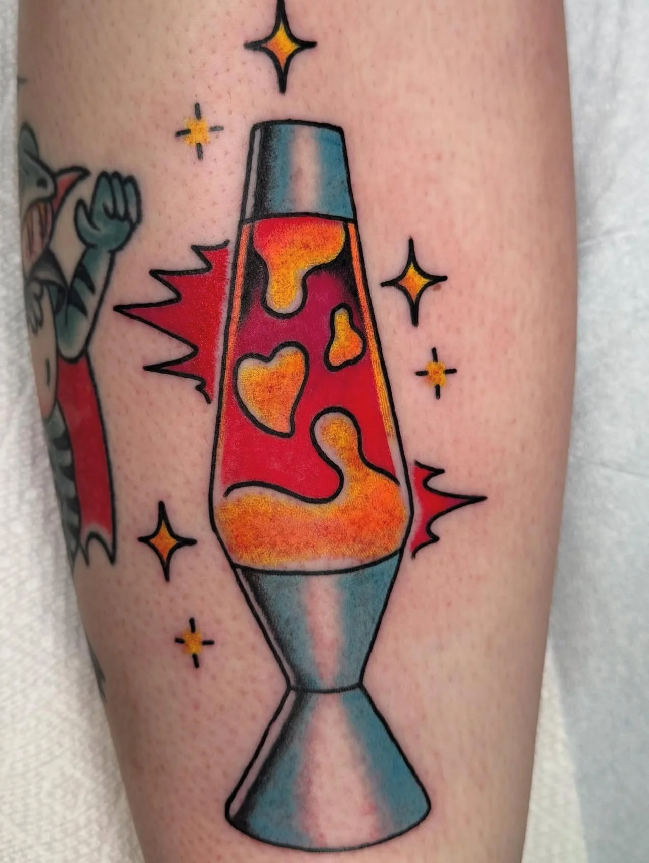 Colorful tattoo of a lava lamp with orange and yellow lava, surrounded by sparkles and stars.