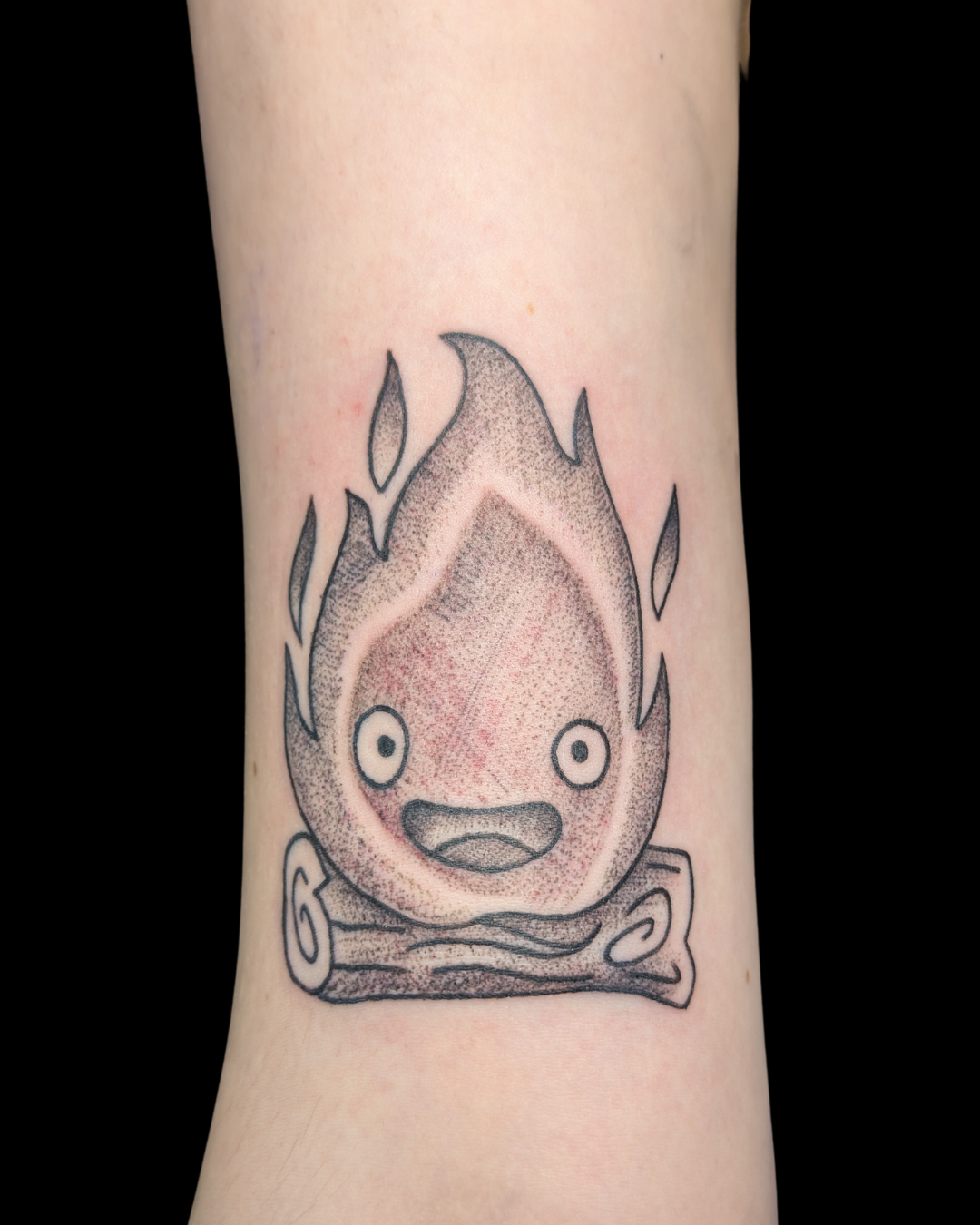 Tattoo of a cartoon clown with green hair, red nose, red cheeks, and a big smile, dressed in a brown jacket, green plaid shorts, and yellow shoes, holding a brown hat.