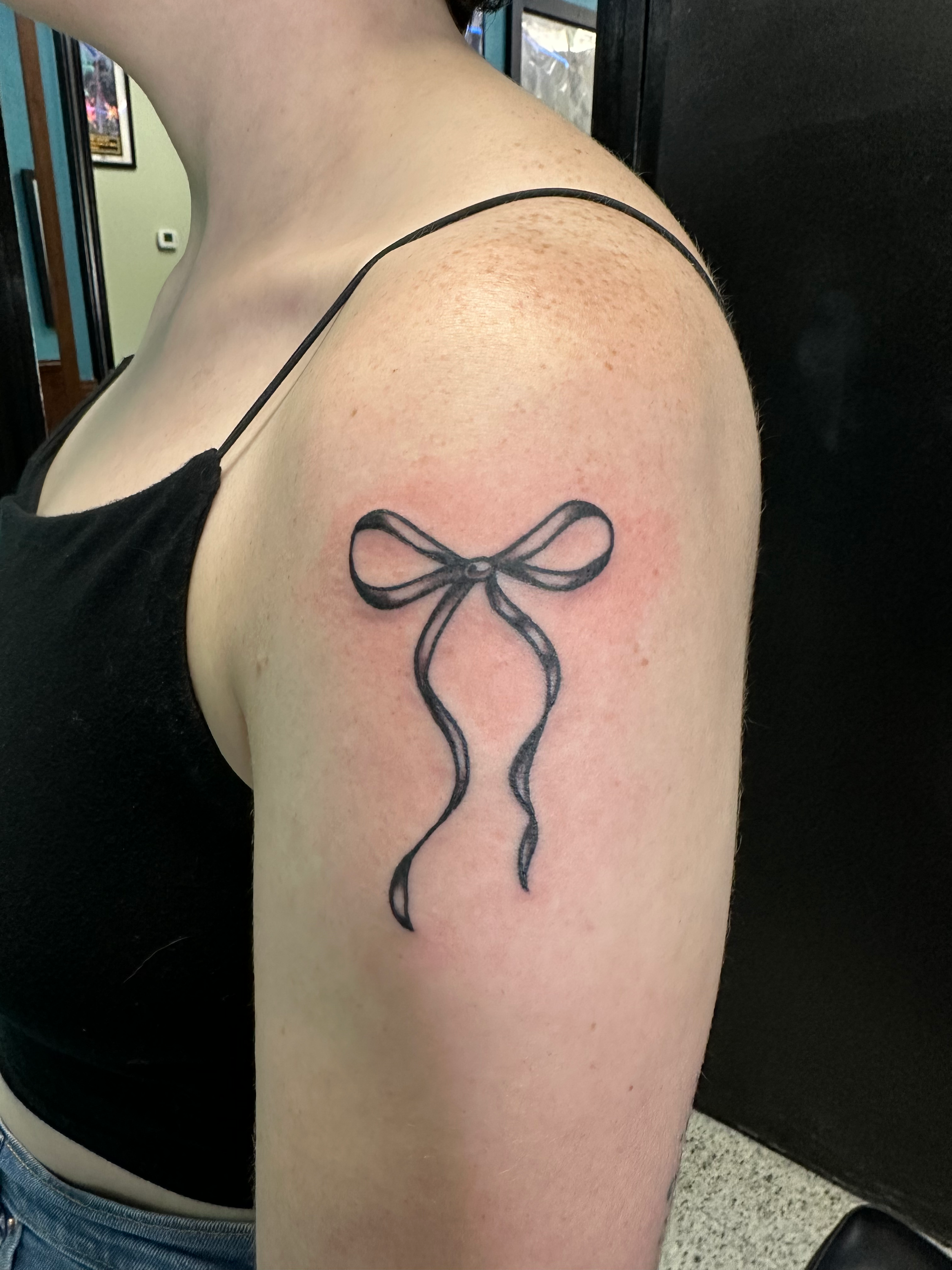 Fine line bow on shoulder by Atlanta tattoo artist Kristin Thorsen at Timeless Tattoo.