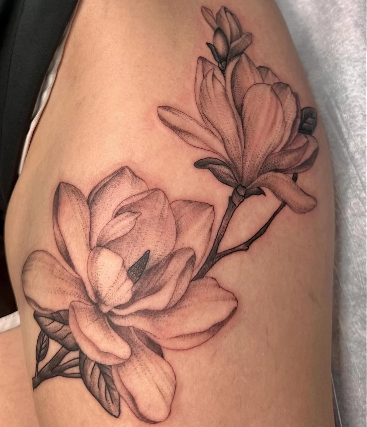 Black and gray floral tattoo featuring large opening flowers and leaves on a person's upper arm.