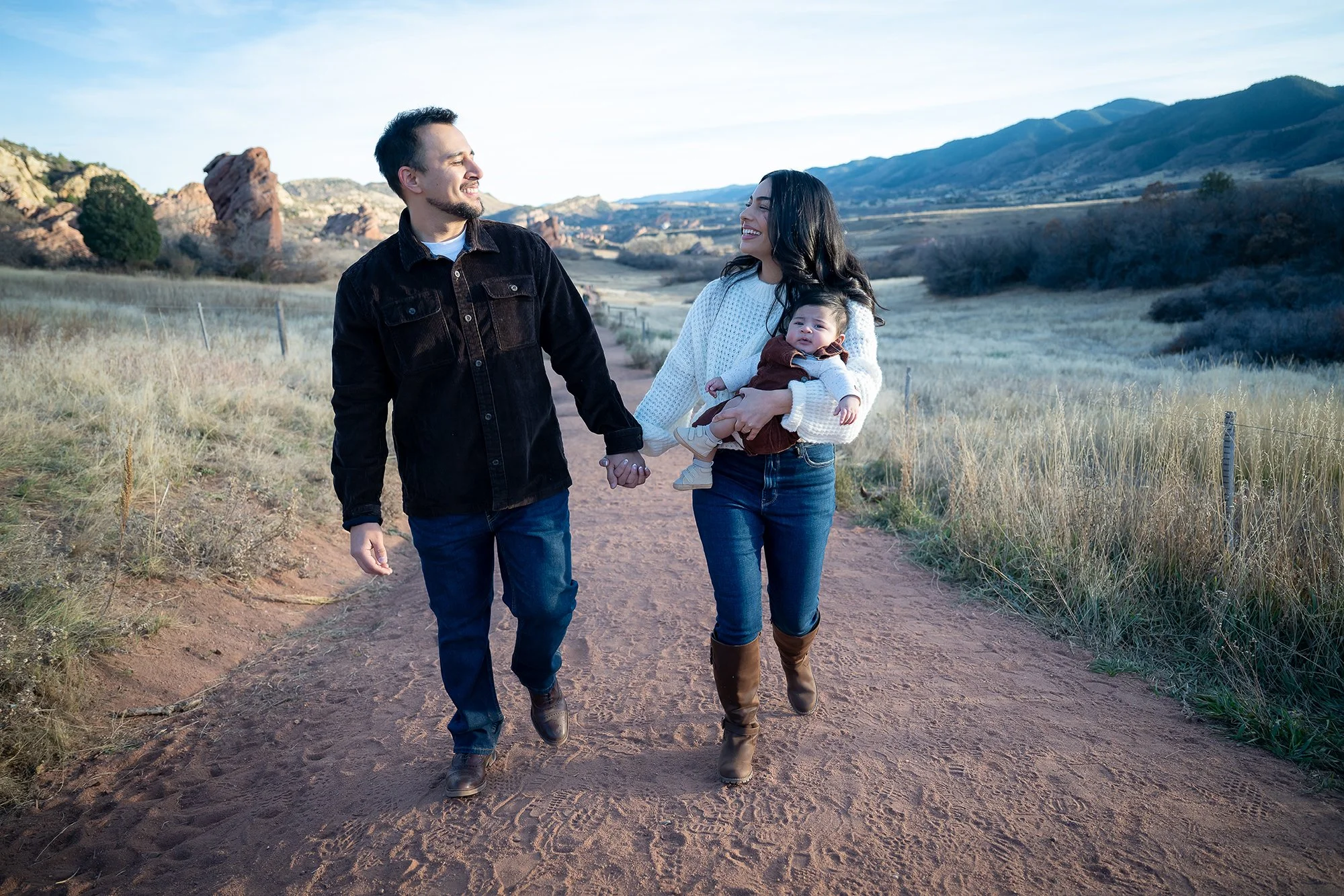 A natural family portrait holding hands walking path with infant son at South Valley Park in Littleton, Colorado captured by Ryan Kost