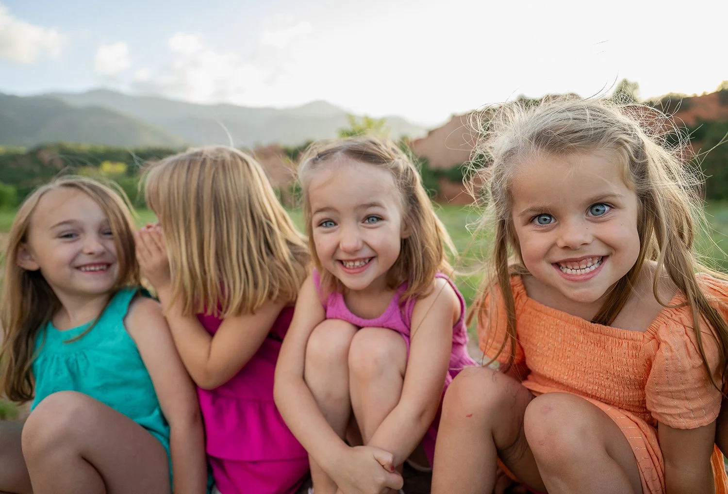Candid summer portrait of four young girls laughing and whispering secrets at Red Rock Canyon Open Space in Colorado Springs, captured by Ryan Kost Photography.
