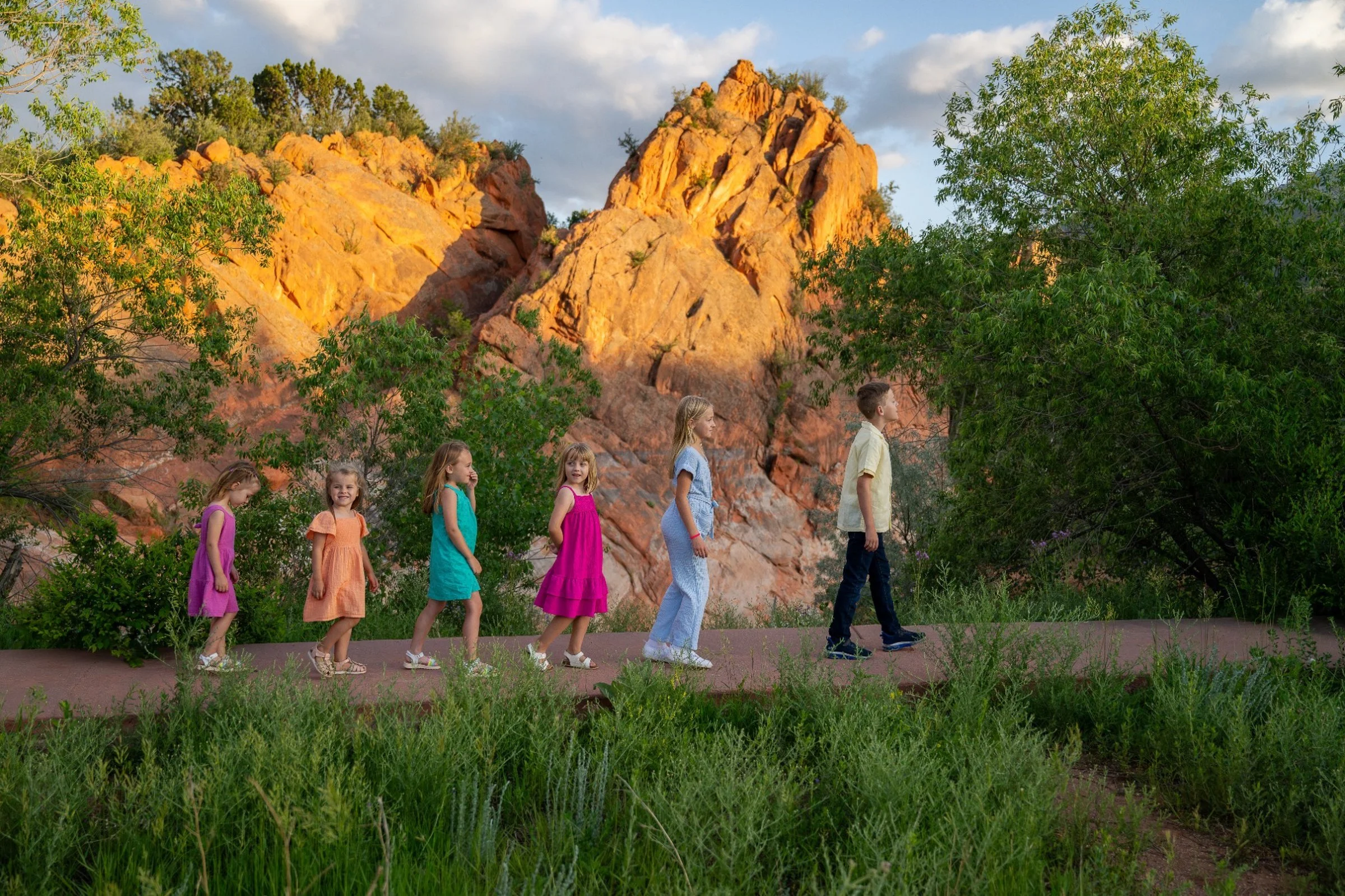 Playful sibling and cousin family photo at Red Rock Canyon Open Space with golden light and dramatic rock formation in background. Genuine, playful moments captured by Ryan Kost.