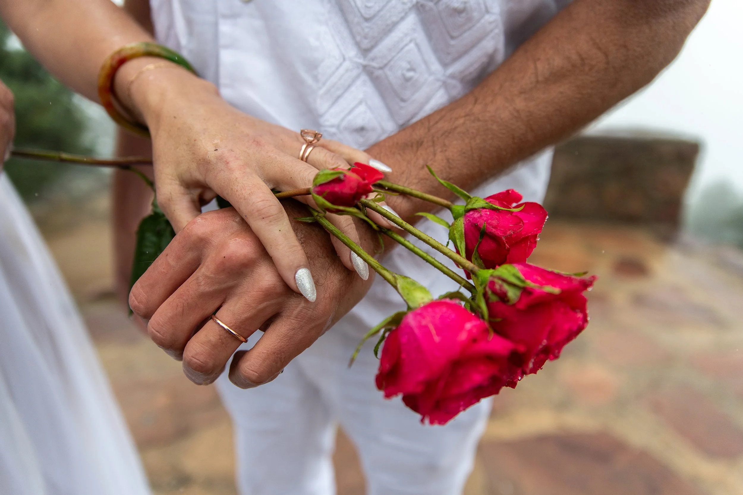 Three pink roses being held by two people, with only their hands and part of their arms visible.