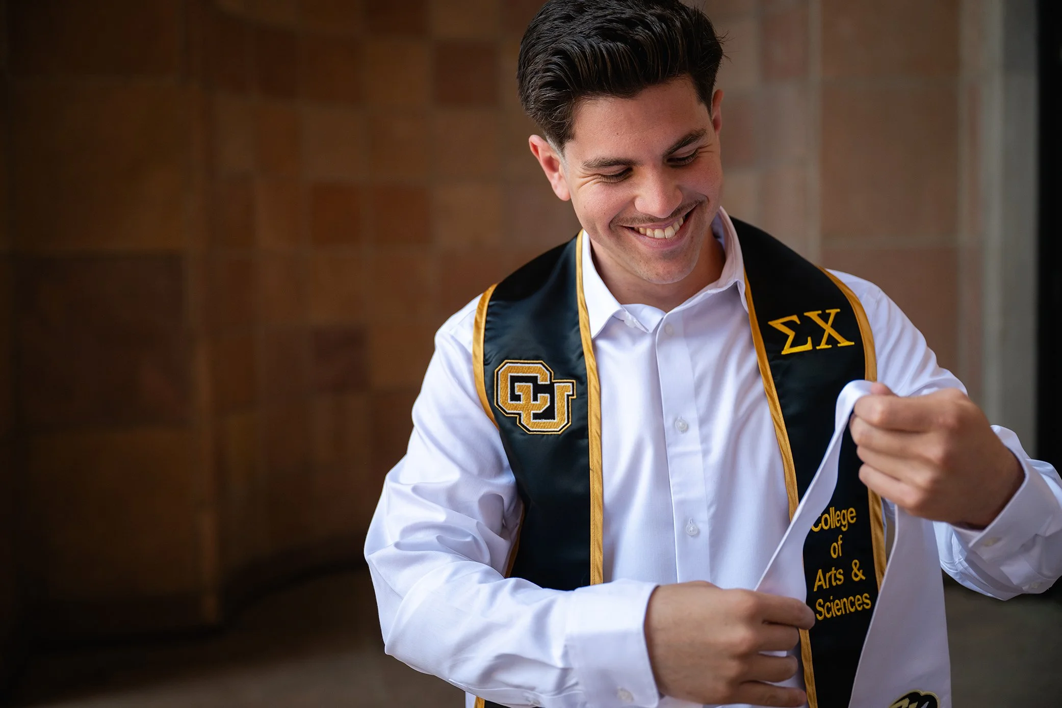 Relaxed graduate portrait of a University of Colorado Boulder student adjusting his fraternity stole on campus