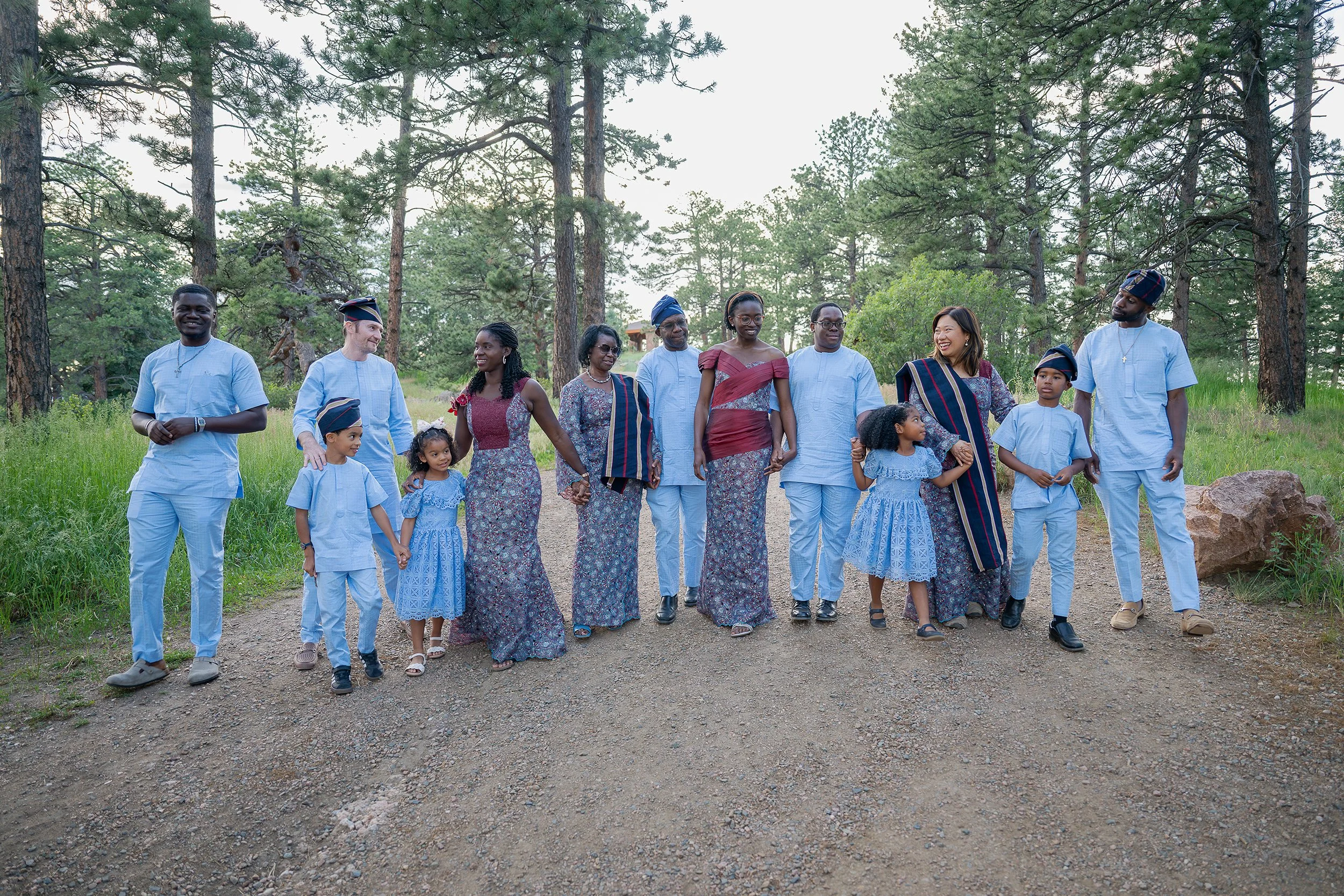 Diverse, multigenerational family walks together holding hands down the trail in summer at Mount Falcon West Trailhead in Colorado. Captured by Denver family photographer Ryan Kost.