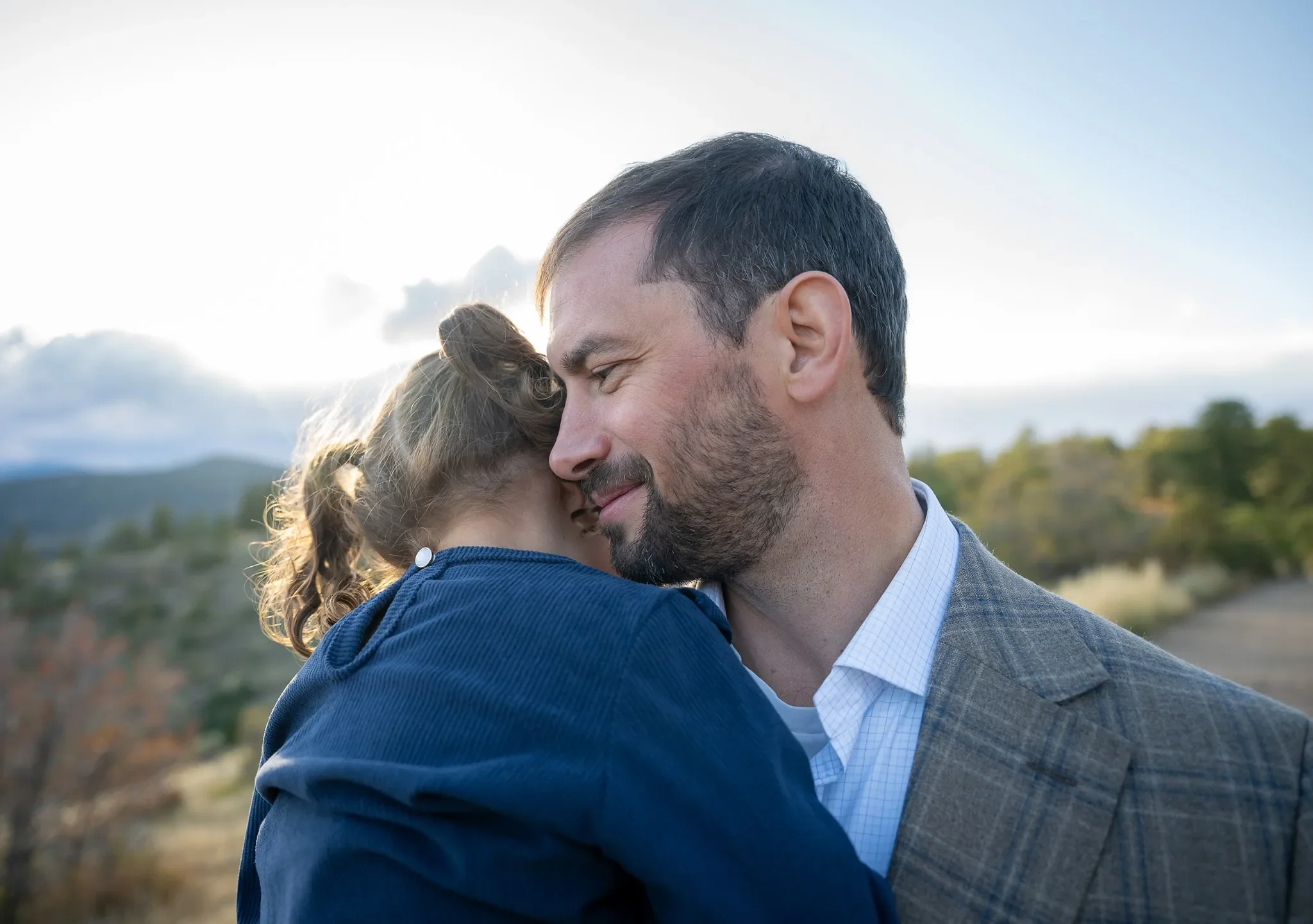 Dad & daughter sweetly hugging while walking the trail during a loving outdoor family photoshoot at Mount Falcon West Trailhead in the Colorado foothills. Ryan Kost Photography
